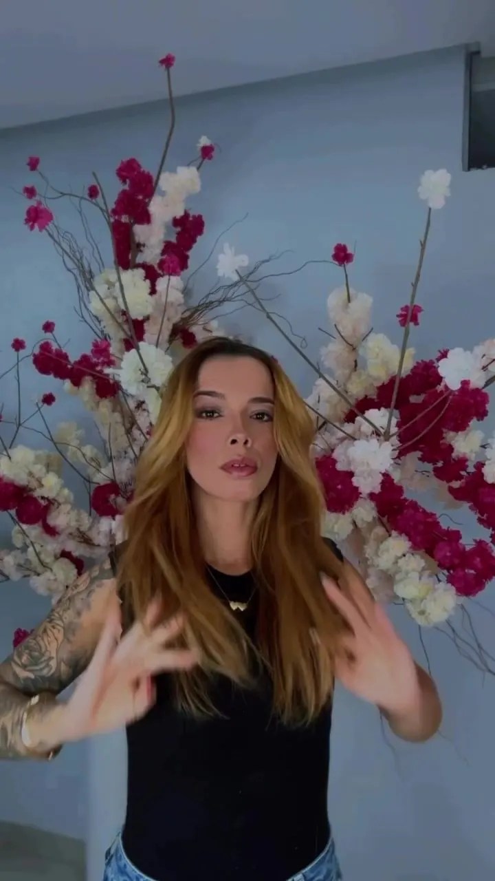 Cliente loira com cabelo liso e longo passando as mãos nos fios diante do arranjo de flores