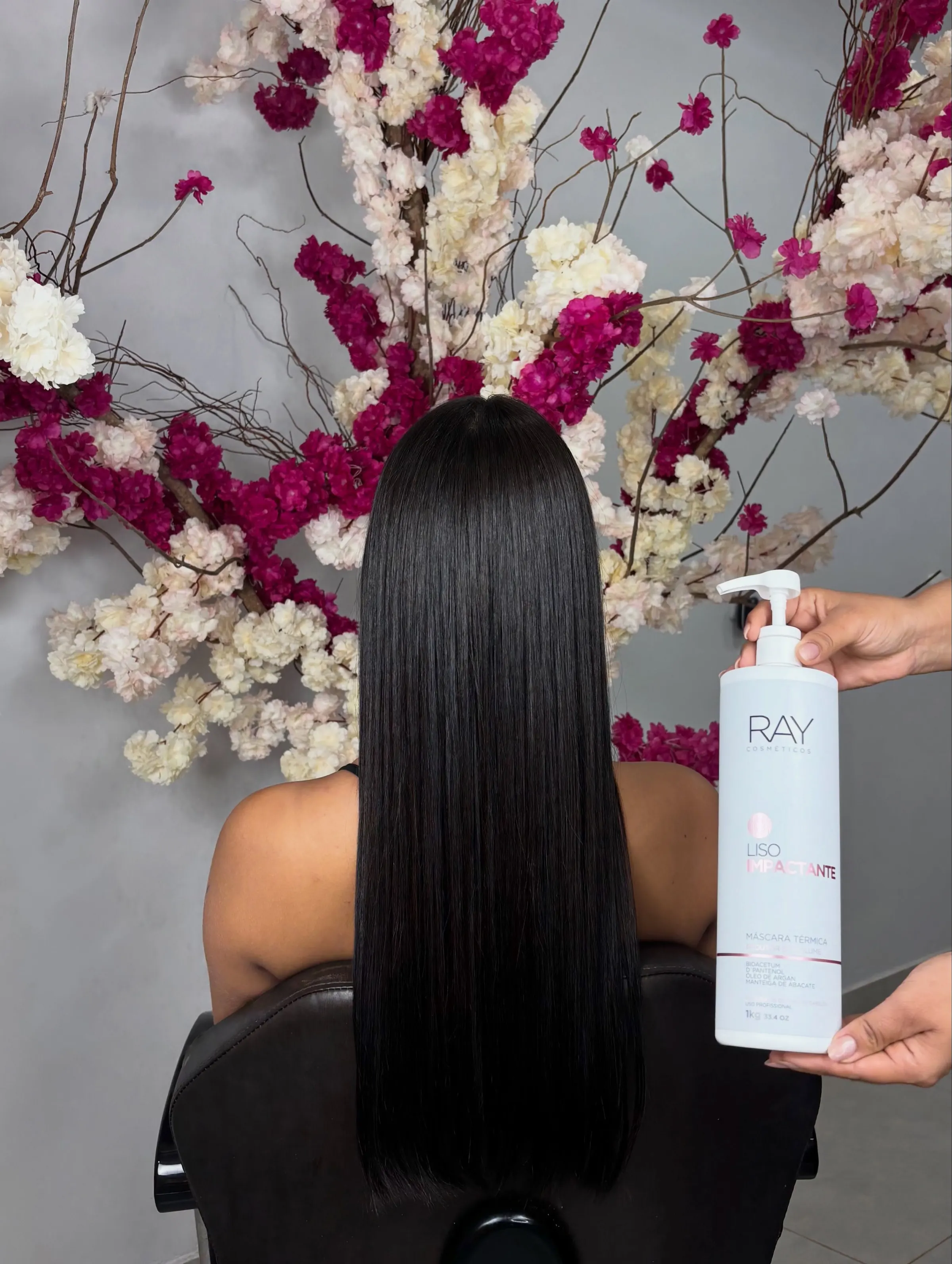 Cliente de costas com cabelo preto, liso e brilhante até a cintura, diante do arranjo de flores do Studio, ao lado da máscara Liso Impactante